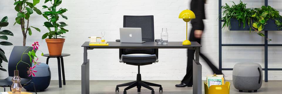 Balance Lift, Well, Recharge 45, 2020 Extra Verta Royal Ahrend Balance Lift workstation in grey with charcoal top and 2020 office chair with female model walking front view
