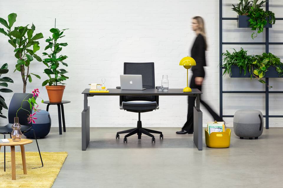 Balance Lift, Well, Recharge 45, 2020 Extra Verta Royal Ahrend Balance Lift workstation in grey with charcoal top and 2020 office chair with female model walking front view