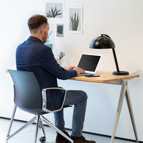 WELL Royal Ahrend Well trestle base chair on castors with polished chrome frame and armrests with anthracite shell and male model with Pyramid table left rear view