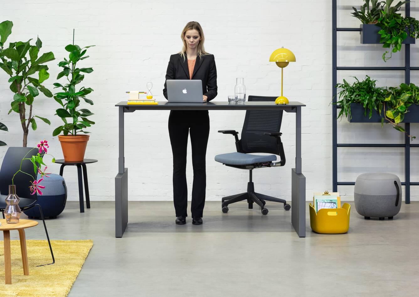 Balance Lift, Well, Recharge 45, 2020 Extra Verta Royal Ahrend Balance Lift workstation in grey with charcoal top in stand position and 2020 office chair with female model standing front view