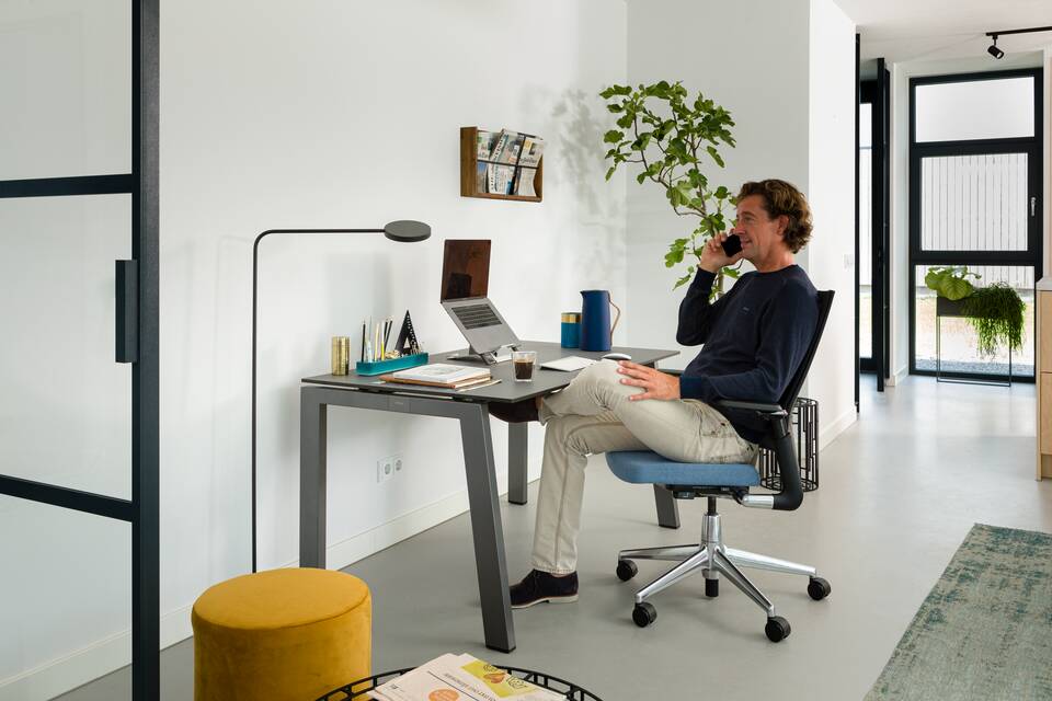 Balance, 2020 Extra Verta Royal Ahrend balance workstation in grey with charcoal tabletop and 2020 Extra Verta office chair upholstered in blue with male model calling interior view
