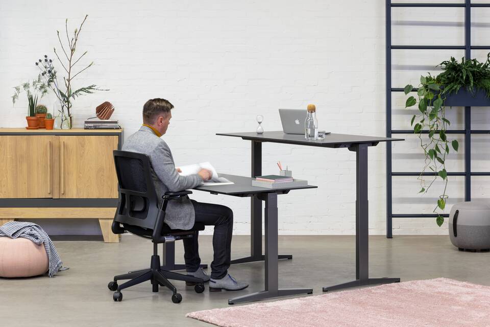 Balance Lift, 2020 Verta, Recharge 45 Royal Ahrend Balance Lift workstations in grey with charcoal tops and 2020 Verta office chair in black with male model front right view